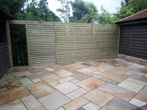 Paved patio area with wooden fencing and greenery in the background.