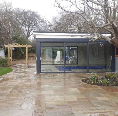 Modern glass extension of a house with stone pathway and a garden area.